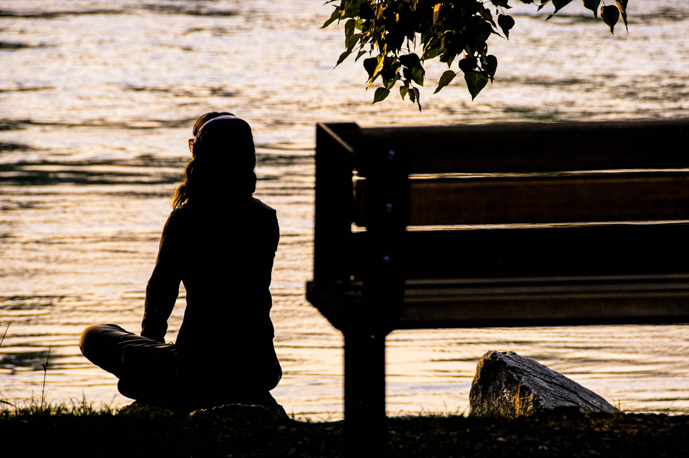 Silhouette einer Person auf einer Bank am Wasser